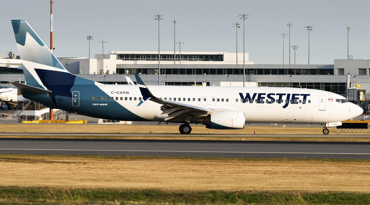 A WestJet Boeing 737 sat on a concrete runway with the airport terminal in the background.