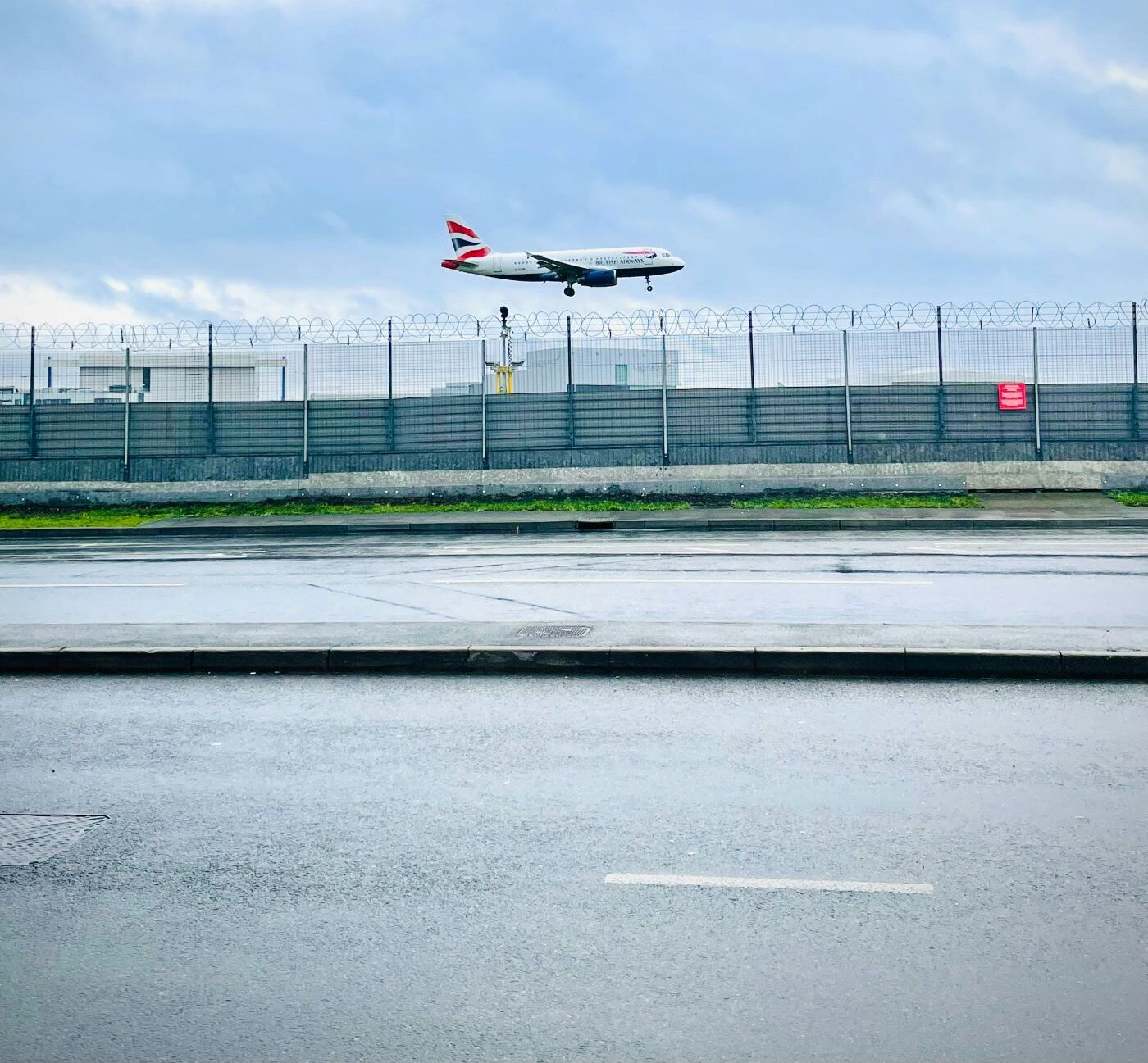 A side view of a plane taking off from a heathrow terminal with a panoramic view of the greytarmac and the green grass seen on the ground and a bright blue sky with white clouds