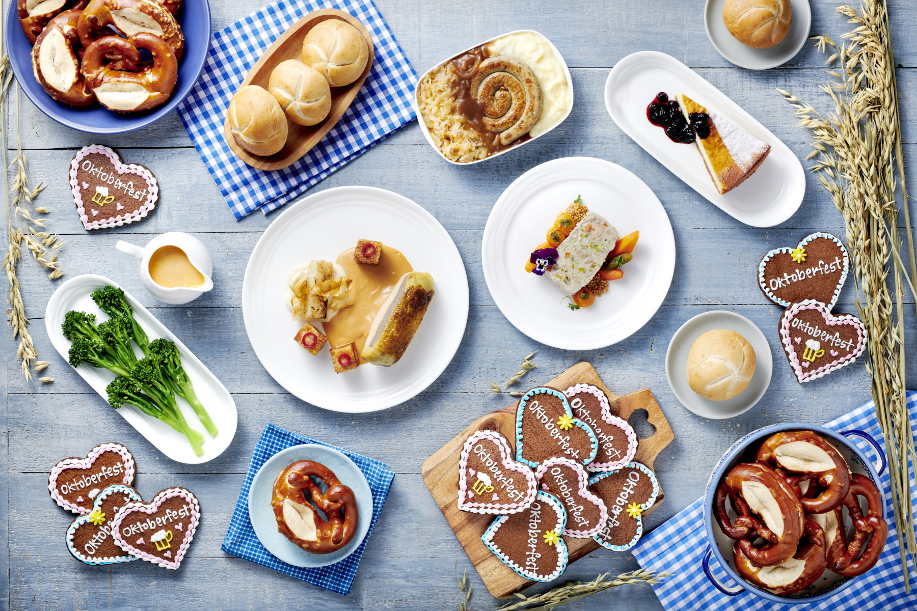 Photograph depicting various Bavarian-inspired food items and wheat on display against the backdrop of a light blue table.