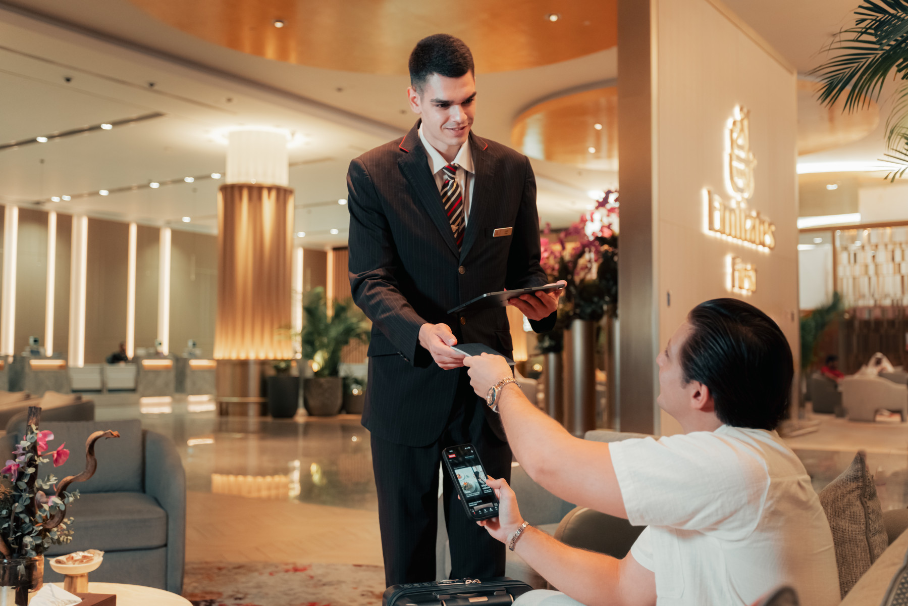 Photograph depicting a man scanning his Emirates app on his phone for Skywards rewards and aided by an Emirates employee
