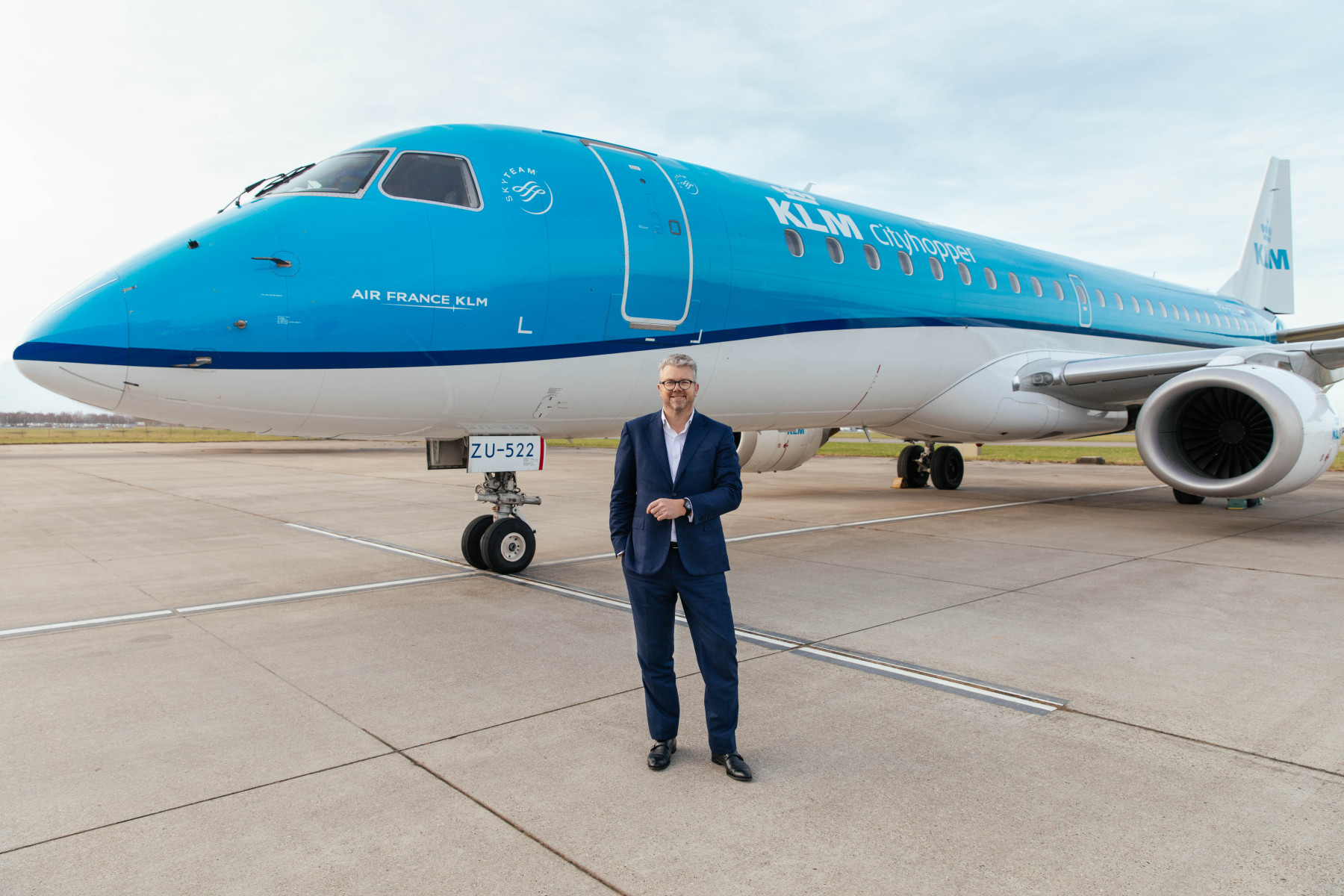 Photograph depicting a man standing in front of a KLM Cityhopper Embraer aircraft.