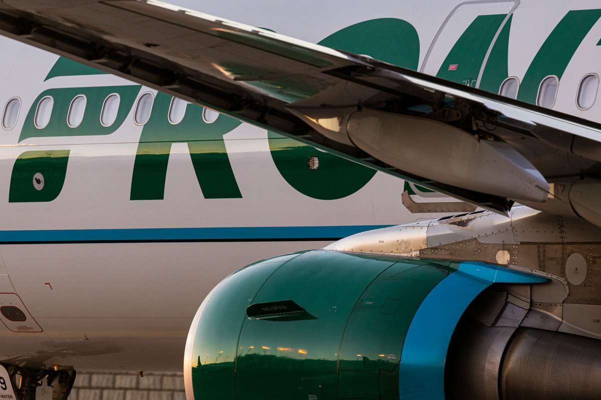 Close-up of a bright green and blue Frontier plane engine located under the wing, with large green letters belonging to the airline's logo visible on the white fuselage in the background.