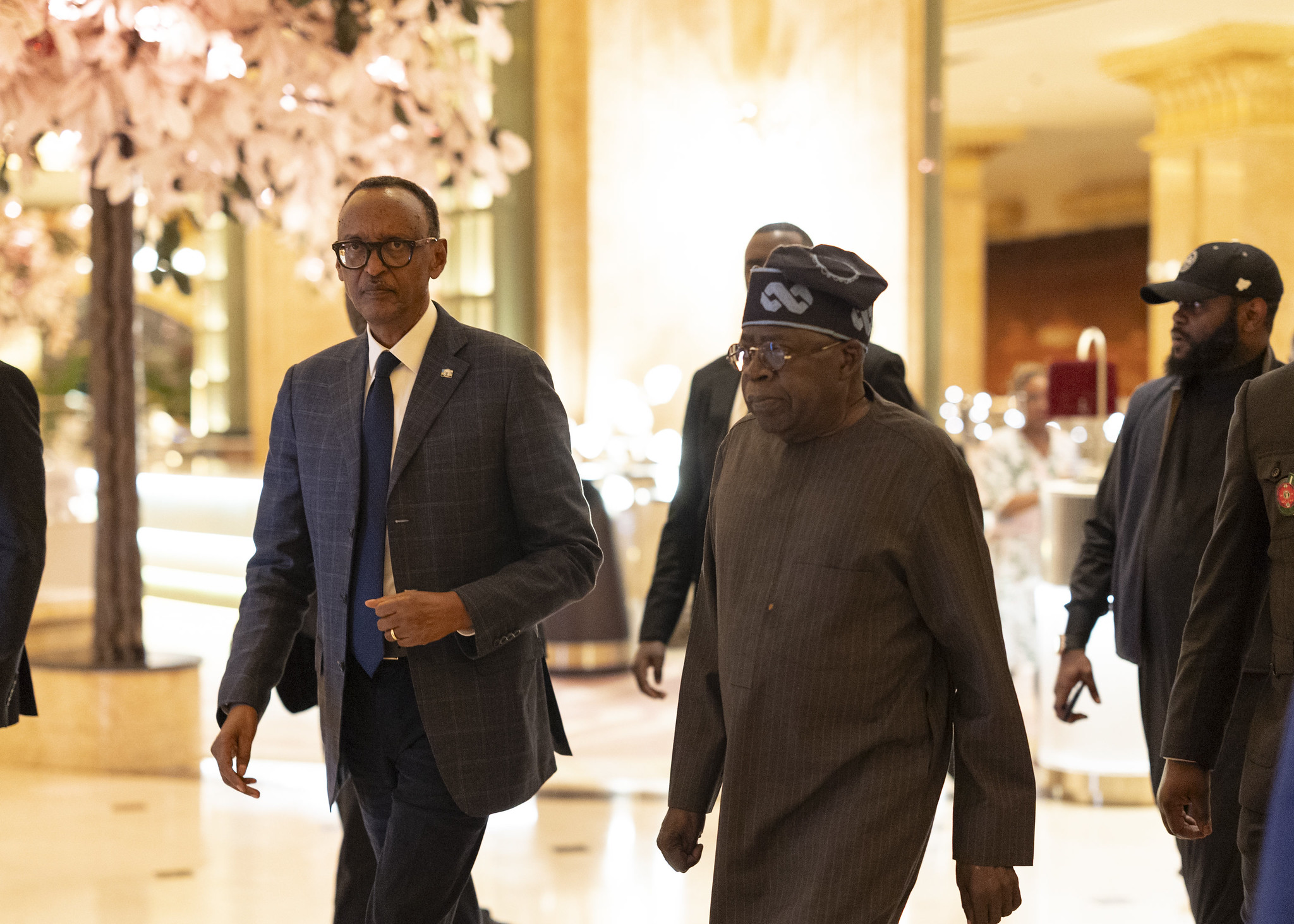 President Bola Ahmed Tinubu of Nigeria, alongside President Paul Kagame of Rwanda. The pair are walking through a well-lit building with marble floors and walls.