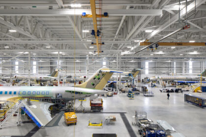 Wide high-angle view inside a bright, vast airplane manufacturing hangar showing multiple commercial aircraft undergoing assembly.