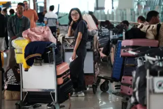 Passengers with luggage trolleys and suitcases waiting inside the departure area of Soekarno-Hatta International Airport during widespread flight disruption.