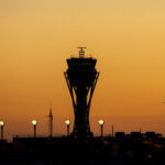 The outline of an Air Traffic Control tower can be seen in front of a sunset illuminated sky. The outline of an aircraft is seen flying away from the tower.