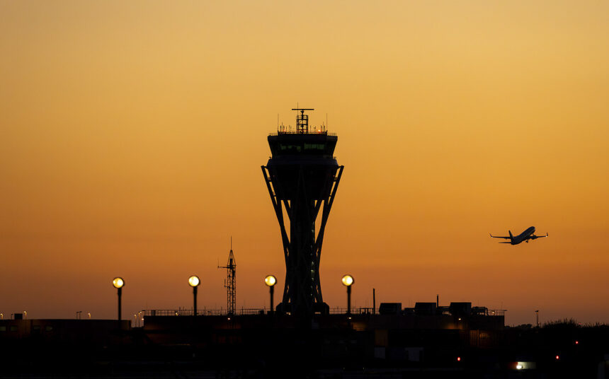 The outline of an Air Traffic Control tower can be seen in front of a sunset illuminated sky. The outline of an aircraft is seen flying away from the tower.