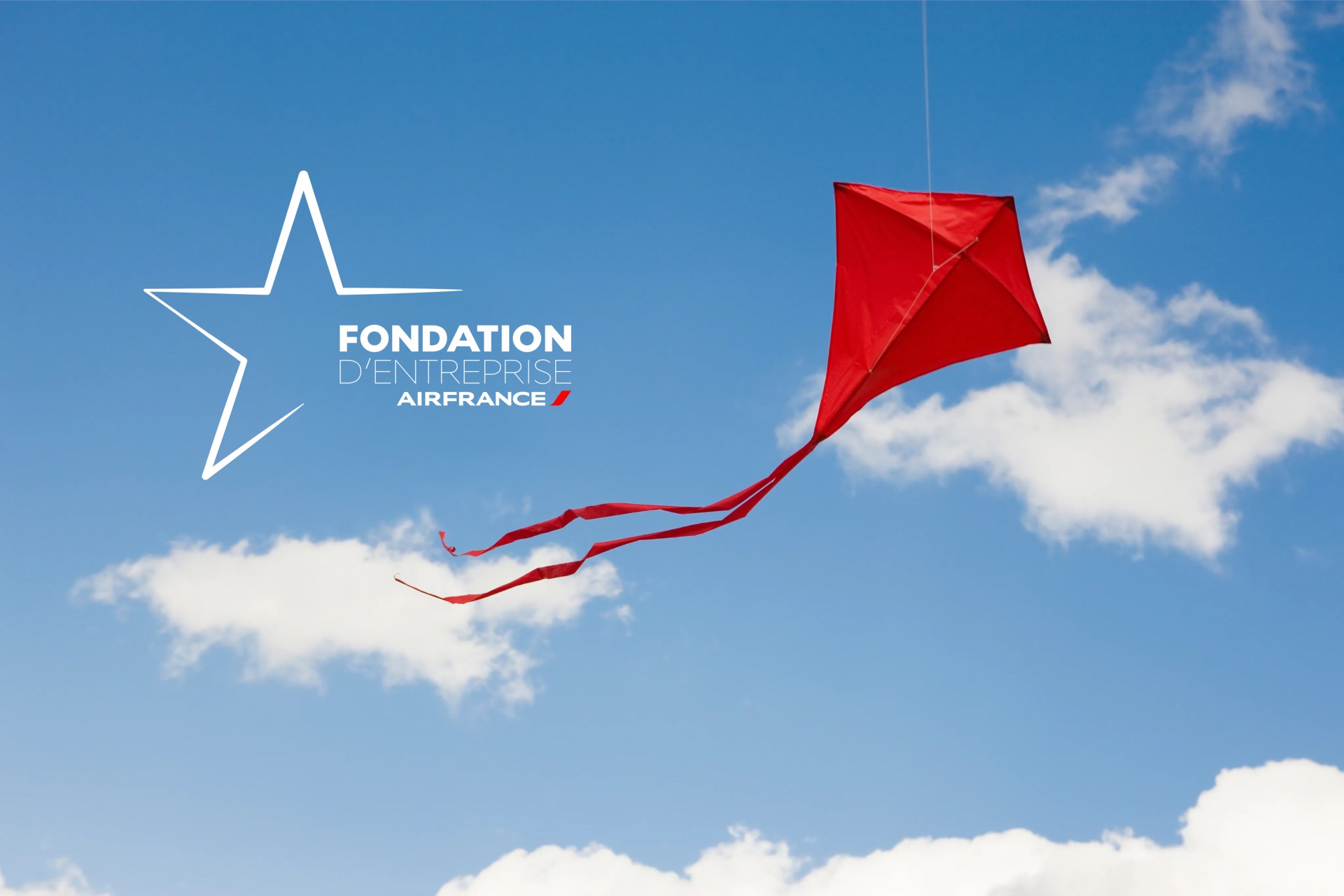 Photograph depicting Air France Foundation logo in French text including a star shape and a red kit flying against the background of a cloudy sky.