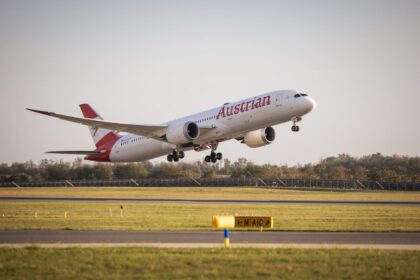 Austrian Airlines B787 taking off into a clear sky. The foreground is grassy