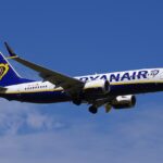 Image depicting a Ryanair Boeing 737 MAX in flight, against a slightly cloudy blue sky.