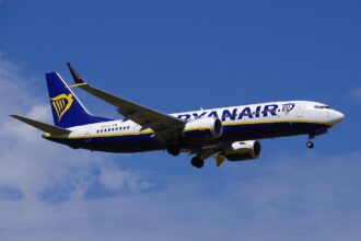 Image depicting a Ryanair Boeing 737 MAX in flight, against a slightly cloudy blue sky.