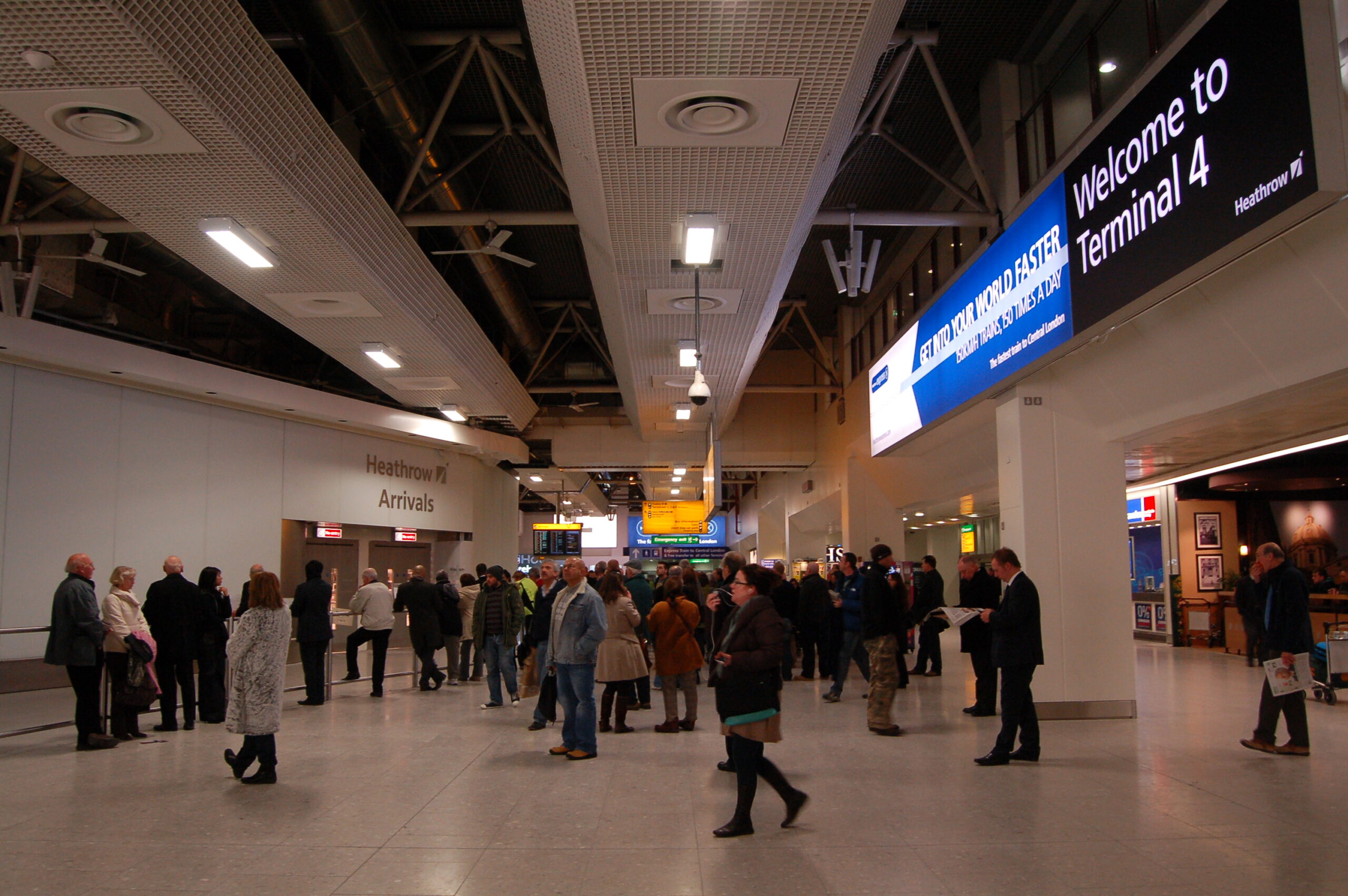 Heathrow's Arrivals hall in Terminal 4, where lots of people are standing around waiting for friends, family and those they know. The interior is white and minimal but lively.