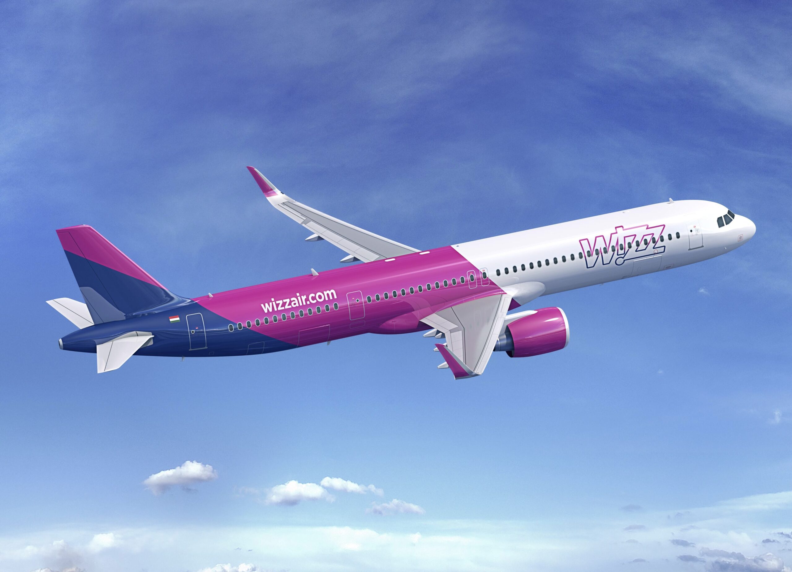 A white, purple, and blue Wizz Air Airbus jet flying upwards in front of a blue sky, above a layer of cloud.
