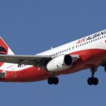 A red and white Air Albania jet flying upwards in front of a clear blue sky.