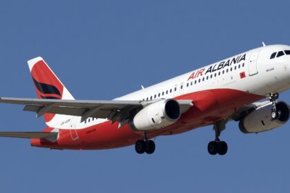 A red and white Air Albania jet flying upwards in front of a clear blue sky.