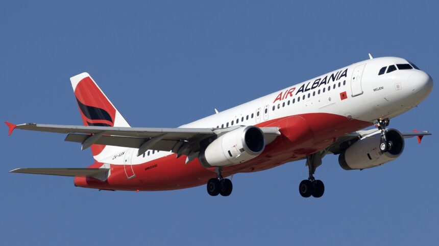 A red and white Air Albania jet flying upwards in front of a clear blue sky.