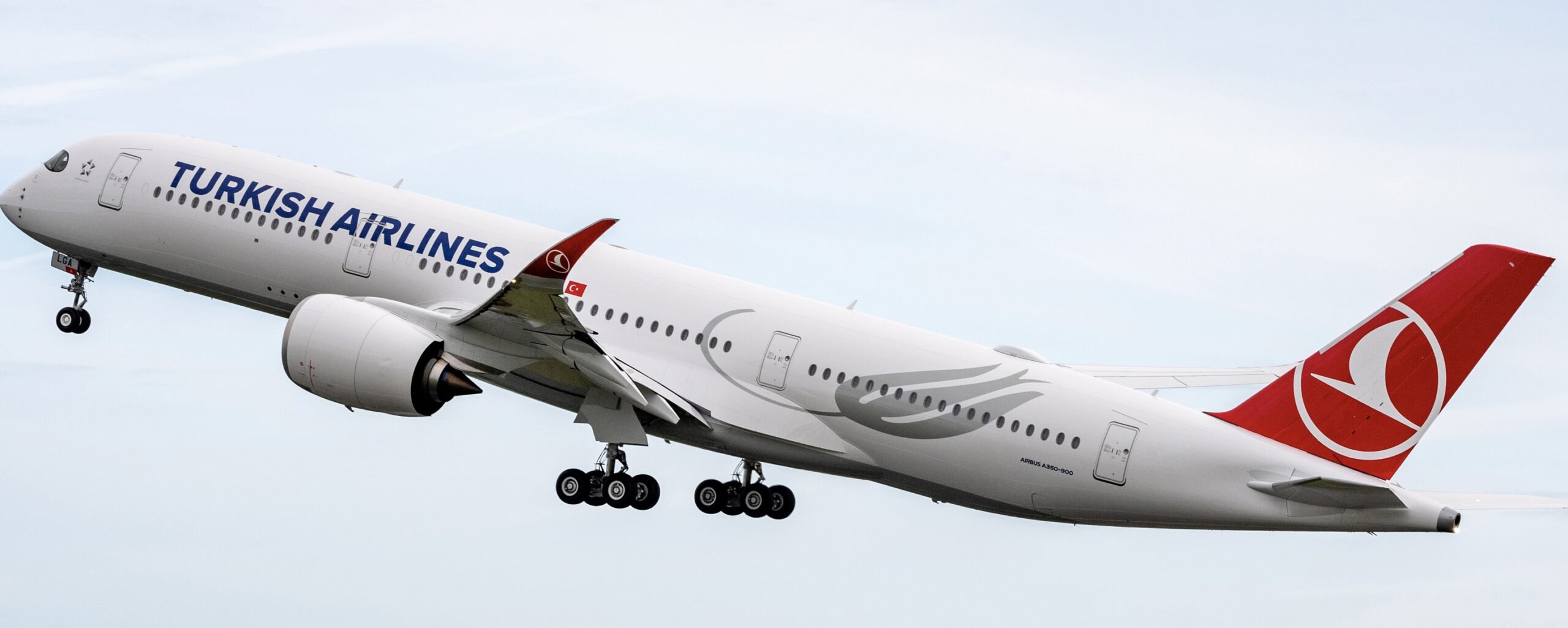 A red and white Turkish Airlines Airbus jet flying upwards in front of a cloudy sky.