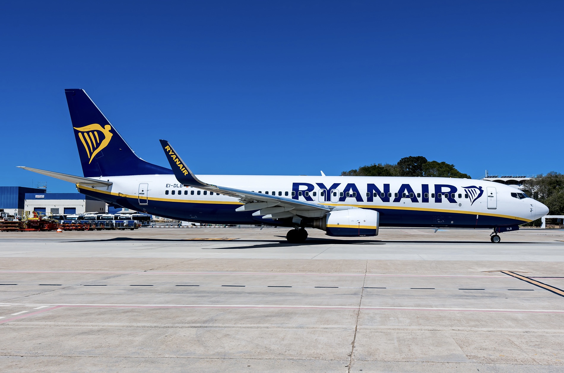 A white blue and yellow Ryanair jet sat on a runway in front of a clear blue sky.