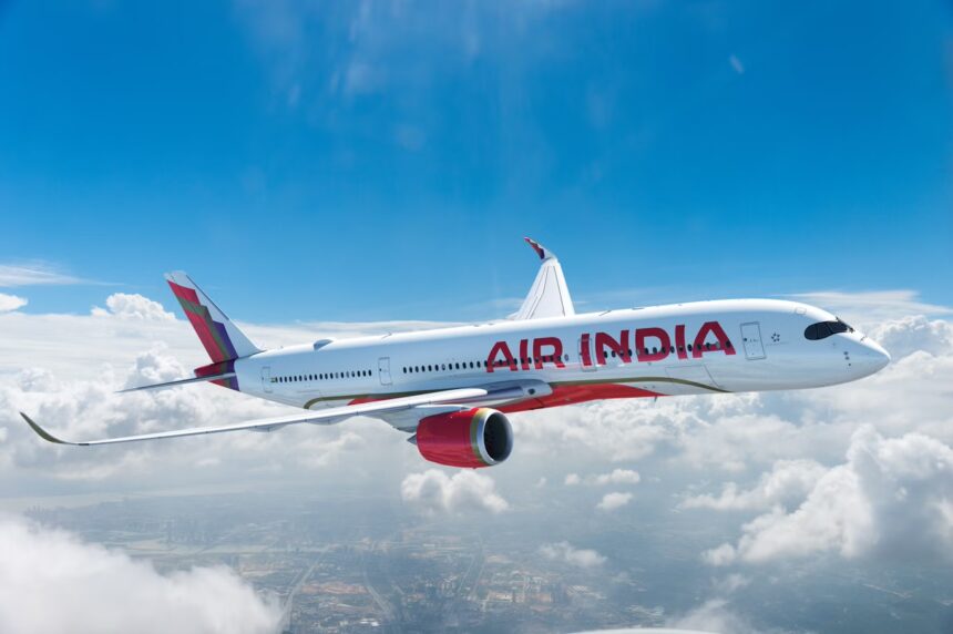 A red and white Air India jet flying over a layer of cloud in front of a blue sky.