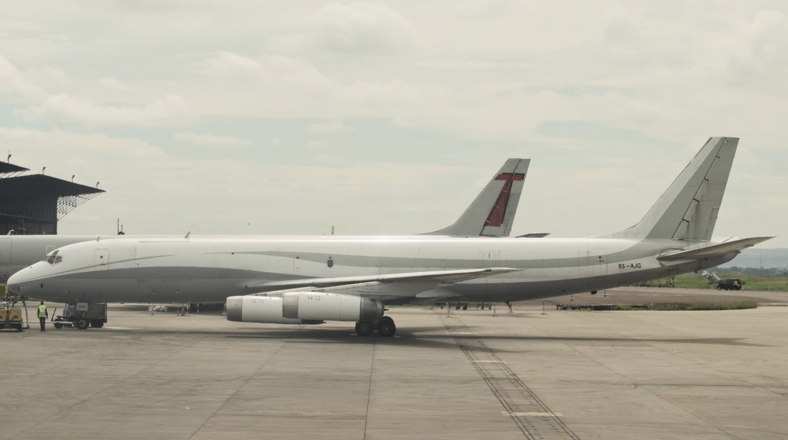 A white and grey TACS jet, sat on an airport runway, beneath a cloudy sky.