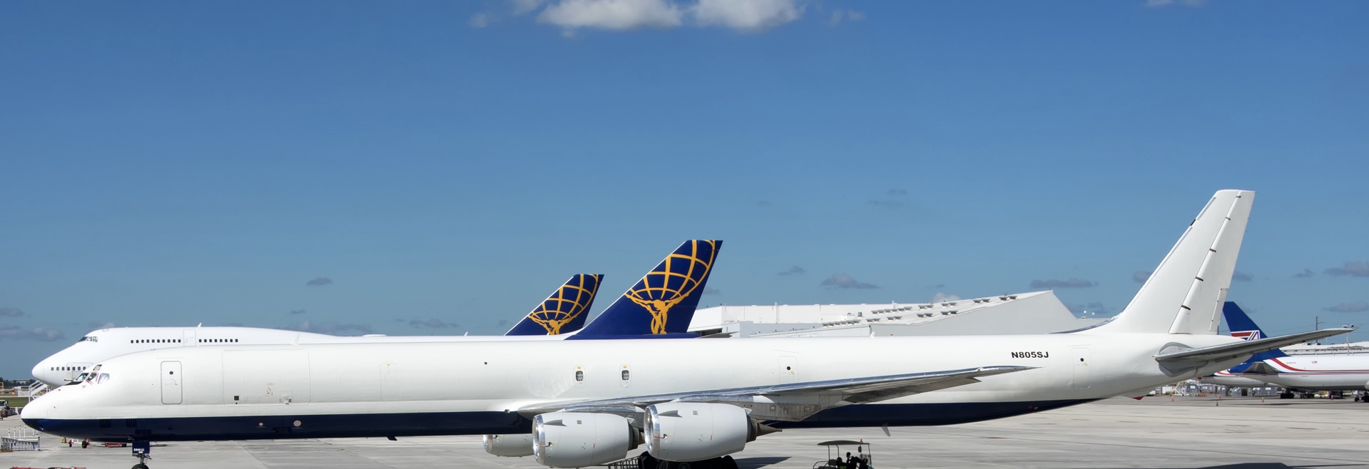 The white, blue, and yellow SkyBus Cargo Charters DC-8-73 jet. The plane is sat on an airport runway, beneath a clear blue sky.
