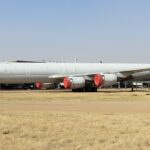 The red and white Douglas DC-8-73, in the livery of Trans Air Cargo Service. The plane is sat on a runway behind a field of yellow grass.