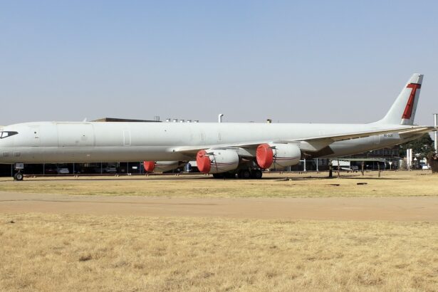 The red and white Douglas DC-8-73, in the livery of Trans Air Cargo Service. The plane is sat on a runway behind a field of yellow grass.
