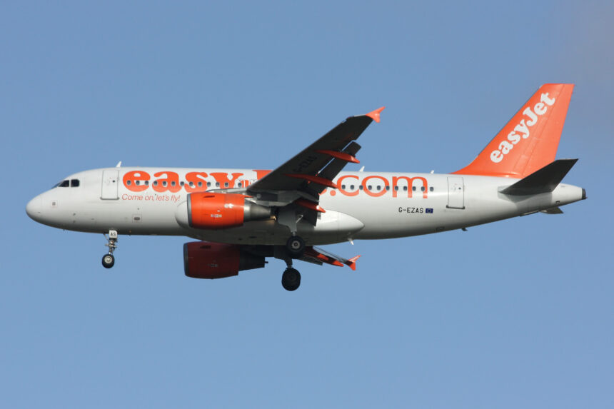 A white and orange easyJet Airbus A319-100 flying in front of a clear blue sky.