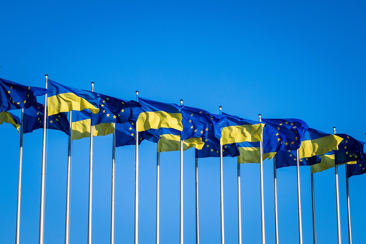A line of Ukrainian and European Union (EU) flags flying in front of a clear blue sky.