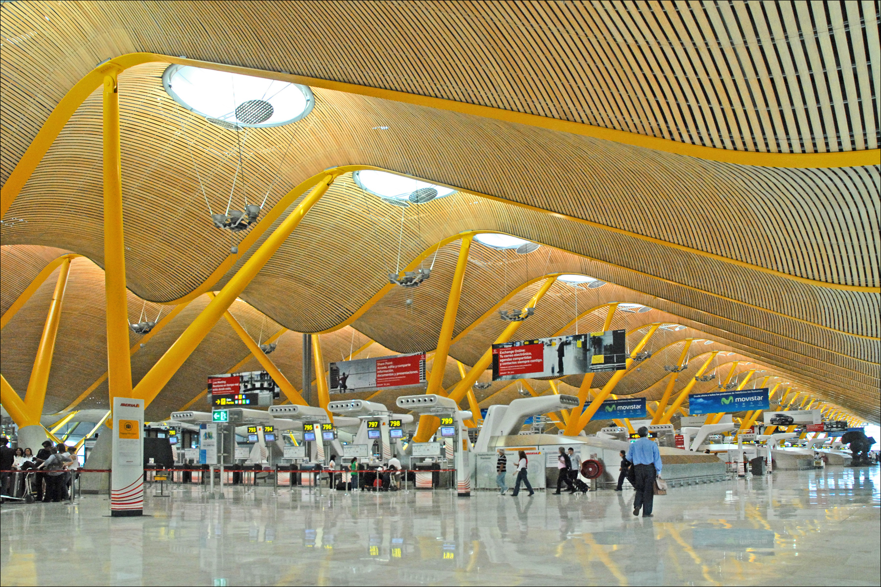 A terminal at Adolfo Suarez Madrid-Barajas Airport (MAD). The terminal is well-lit, with a sloping roof.