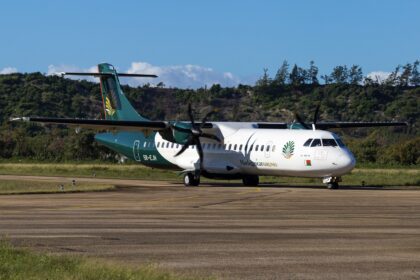 An ATR 72 jet in the green and white livery of Madagascar Airlines. The jet is sat on a runway in front of a small forest, on a clear day.