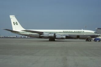 A green and white Nigeria Airways jet sat on a runway in front of a clear blue sky.