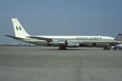 A green and white Nigeria Airways jet sat on a runway in front of a clear blue sky.