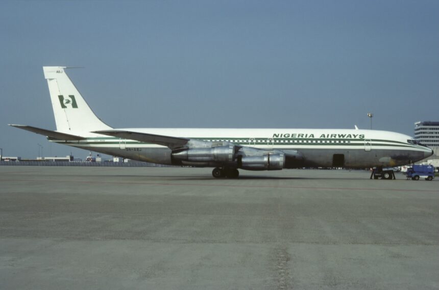 A green and white Nigeria Airways jet sat on a runway in front of a clear blue sky.
