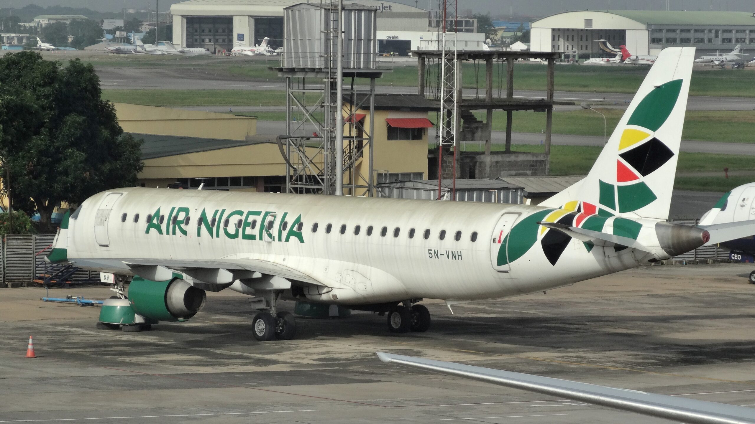 A white and green Air Nigeria jet sat on a runway. A terminal building is visible behind the aircraft.