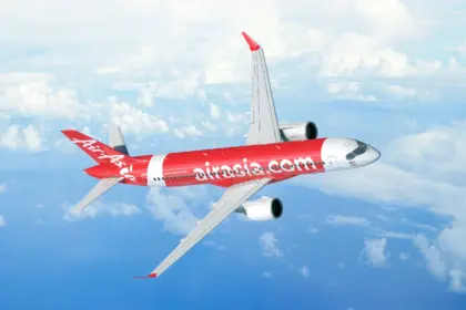 A red and white AirAsia jet flying over an ocean. A few clouds can be seen below the jet.