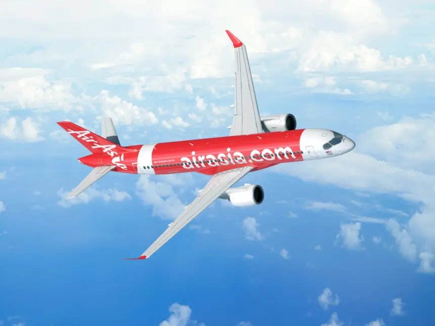 A red and white AirAsia jet flying over an ocean. A few clouds can be seen below the jet.