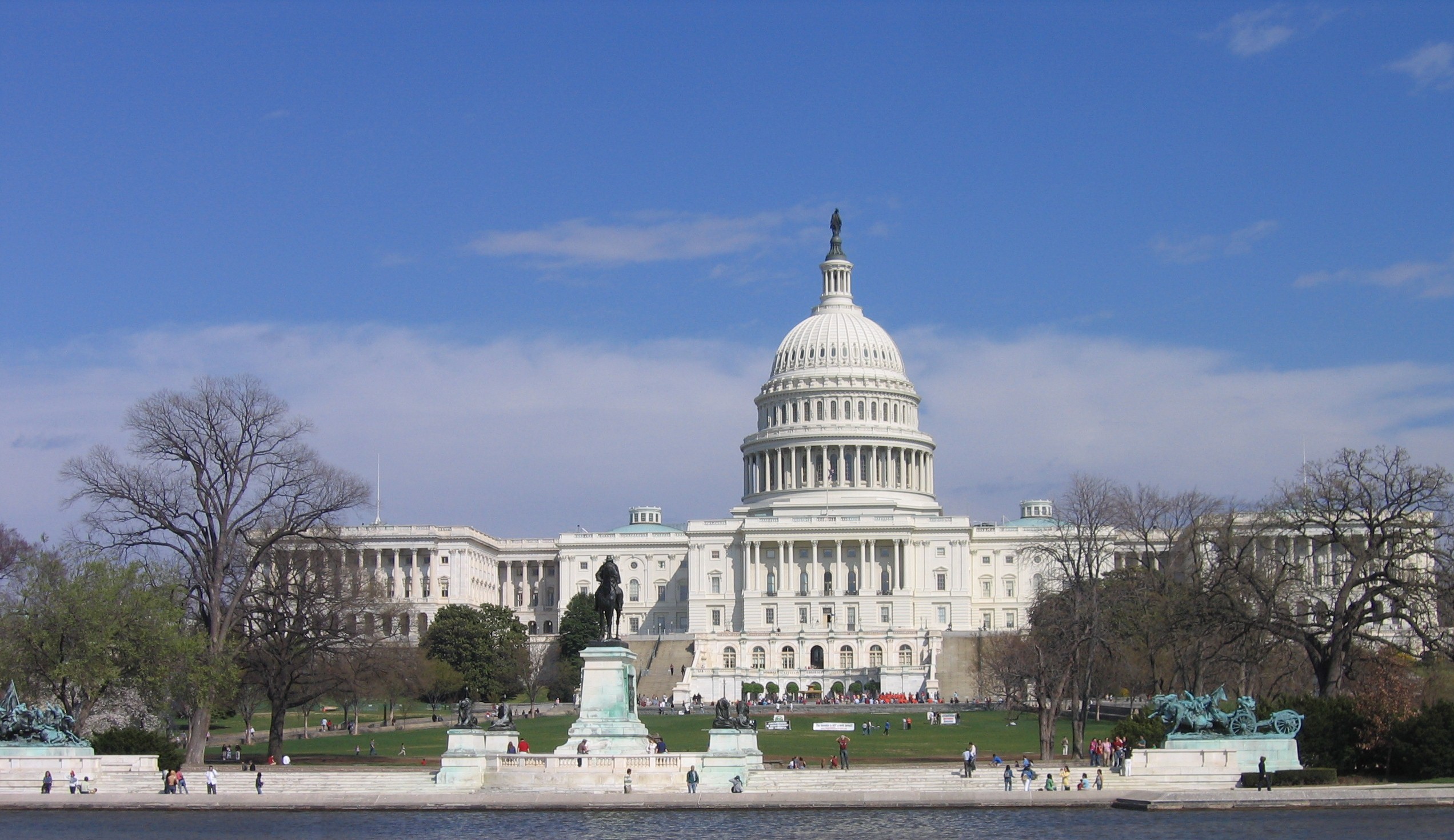 The US congress building on Capitol Hill in Washington, shown behind a green lawn and a pair of trees.