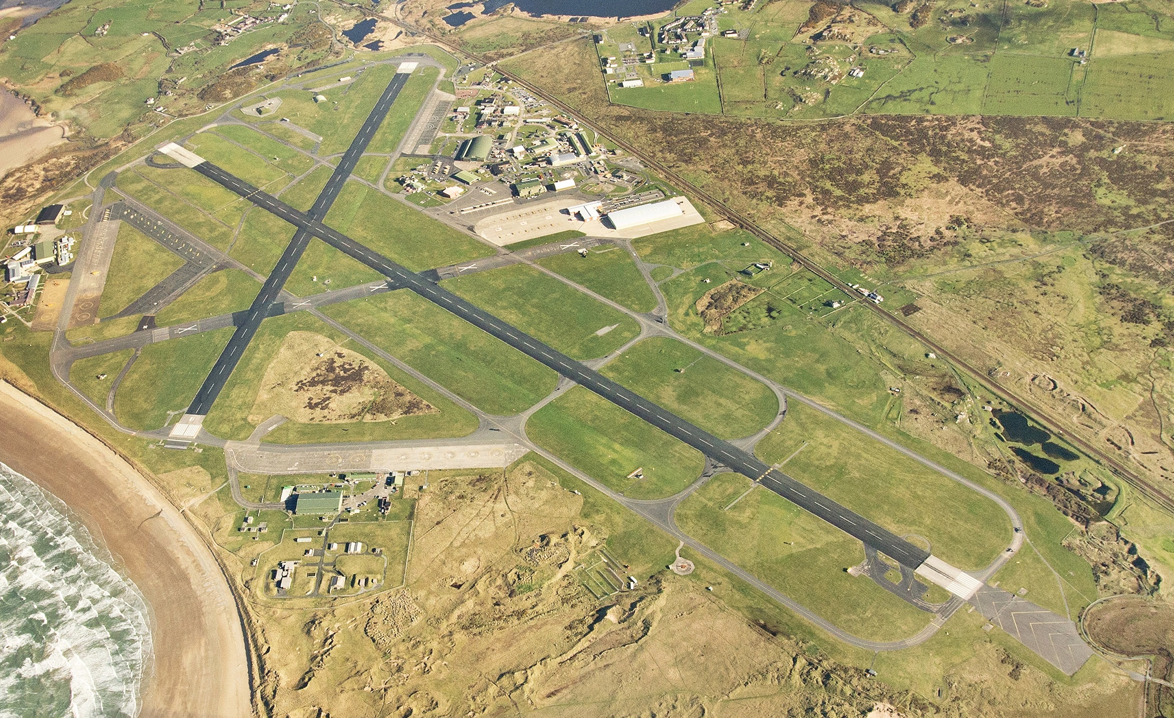 An aerial shot of RAF Valley on the Isle of Anglesey in North Wales. Two black runways cut across a light green field.