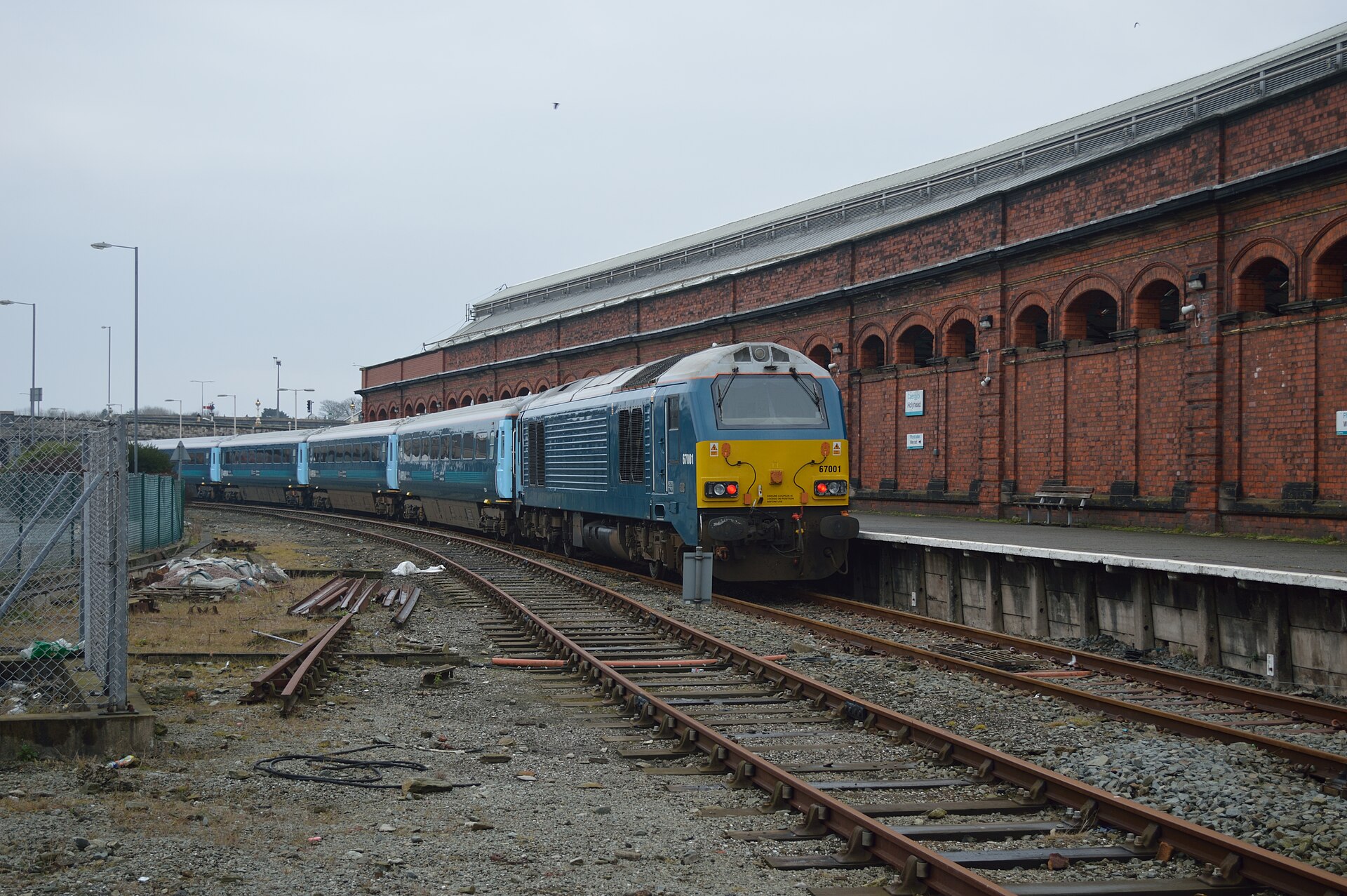 A yellow and blue Arriva locomotive sat outside an orange brick building at Holyhead station in Anglesey.