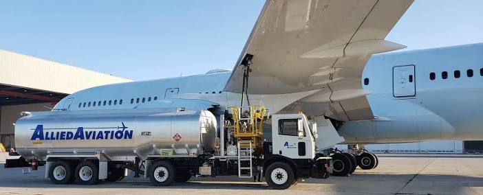 A fuel tanker with “Allied Aviation” written on the side supplying fuel to a white aeroplane.