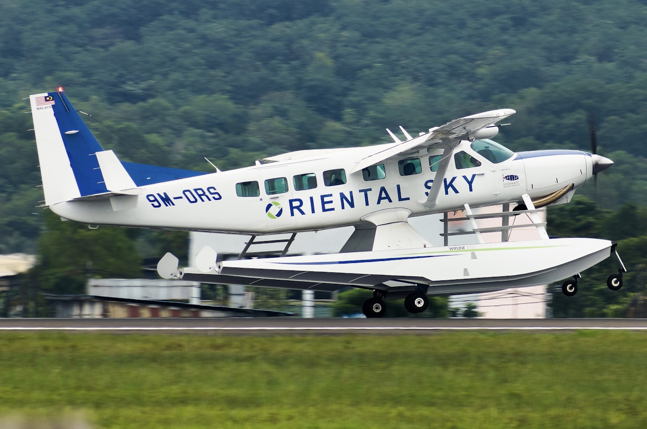A white Oriental Sky plane taking off from an airport runway behind a verge of green grass.