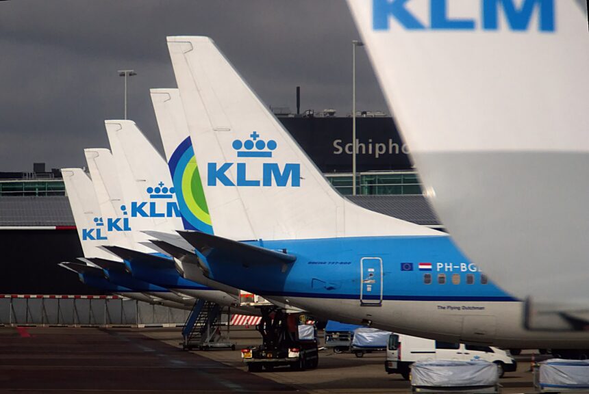 Several KLM aircraft tails are pictured lined up in a row at Schiphol Airport in Amsterdam, getting further away from the photographer. The tails are white, with mid blue underbellies and KLM branding on the tail in the centre.