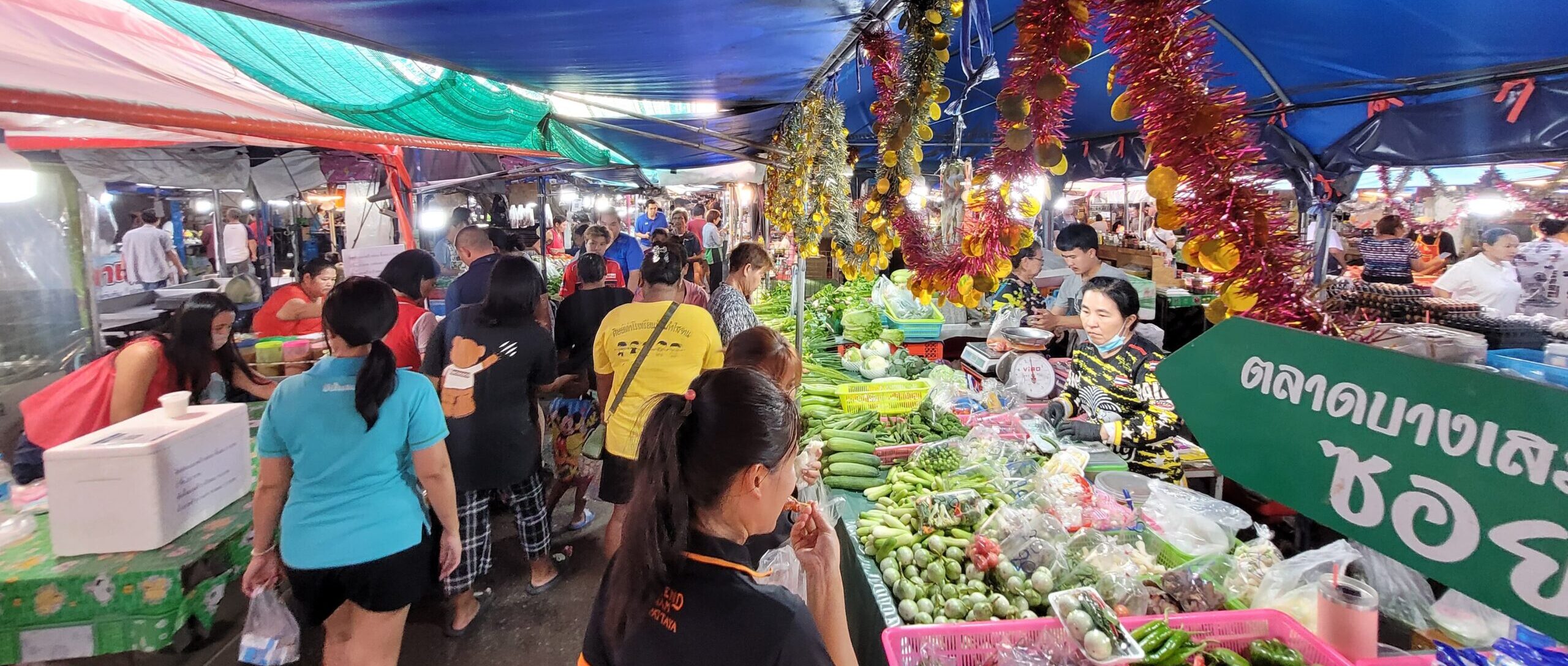 Image shows a busy street market in Thailand with shoppers perusing the local produce