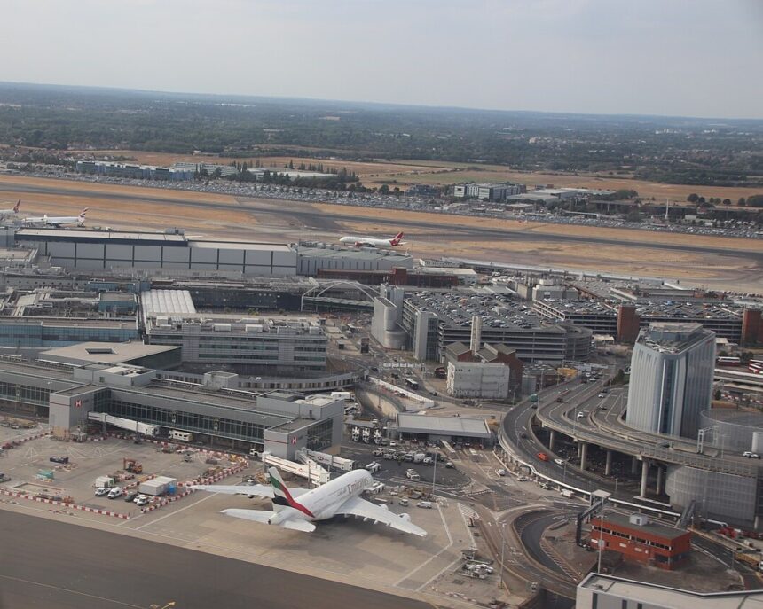 A part of London's Heathrow International Airport with a couple planes stationed around. The grass around the runway is dry and yellow. The airport has an air of busyness despite it not being entirely visible.