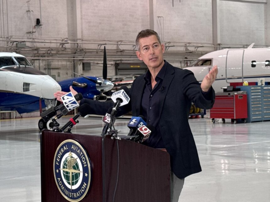 Sean Duffy speaking at a podium bearing the Federal Aviation Administration seal inside an aircraft hangar with planes visible in the background.