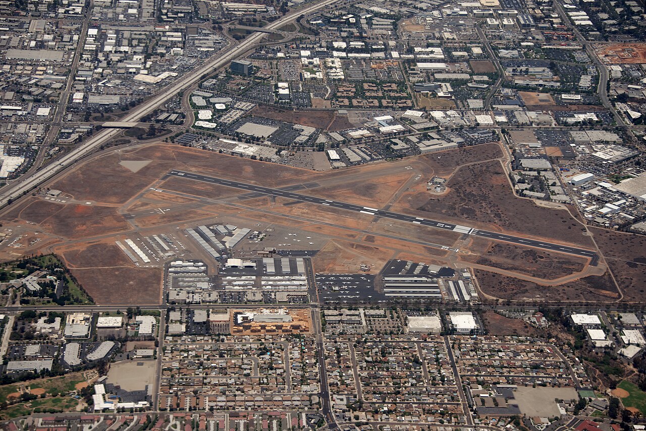 Aerial photograph of Montgomery-Gibbs Executive Airport. The airstrips can be seen near the centre of the image, above the main buildings of the airport, surrounded by bare brownish ground. Beyond, residential areas can be seen around the airport. 