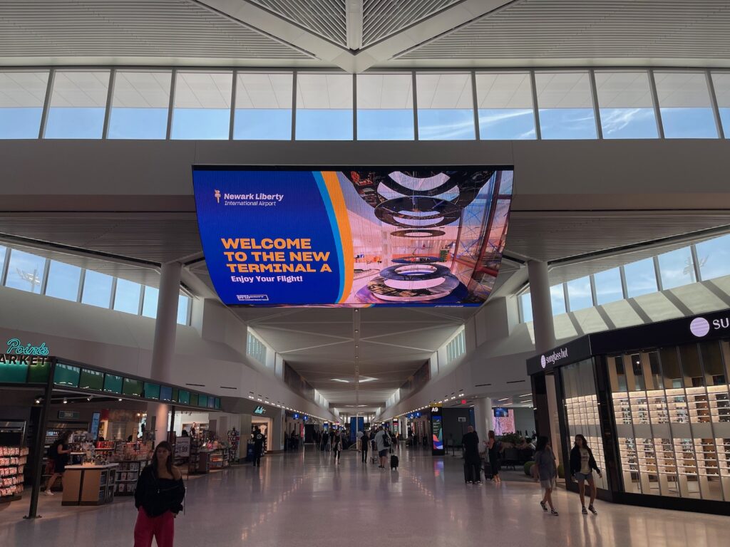 Large screen displaying "Welcome to Newark Liberty Airport Terminal A" with an airport background.