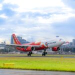 Vietjet aircraft on a green grass field with buildings at the back