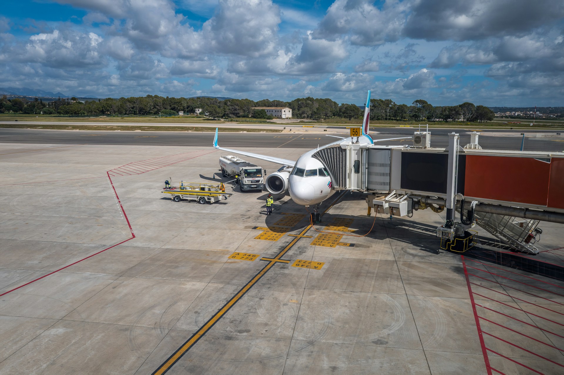An airplane is connected to a jet bridge in the airport with trucks next to it